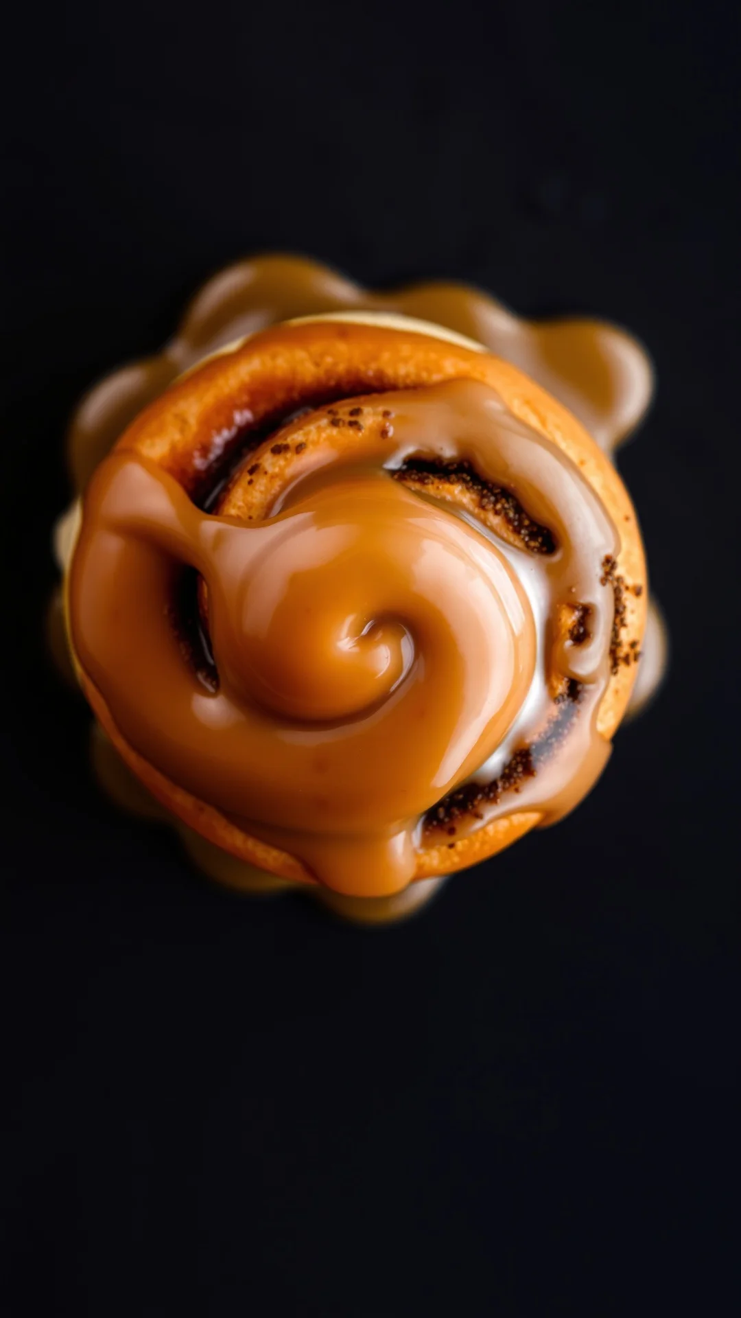 Close-up overhead shot of a single warm cinnamon roll with flowing caramel glaze and cream, swirled spiral texture, macro foo