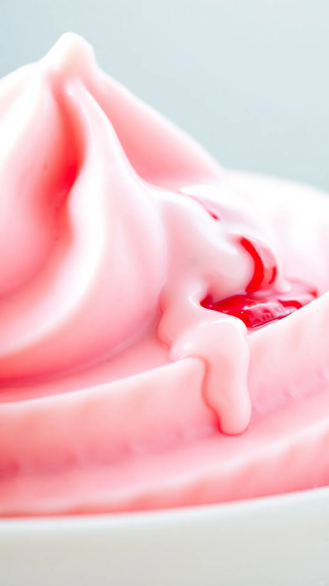 Close-up macro shot of creamy pink strawberry ice cream with whipped texture, fresh strawberry pieces visible, dripping motio