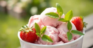 Homemade strawberry ice cream in a bowl, topped with fresh strawberries and mint leaves, creamy pink color, outdoor summer se